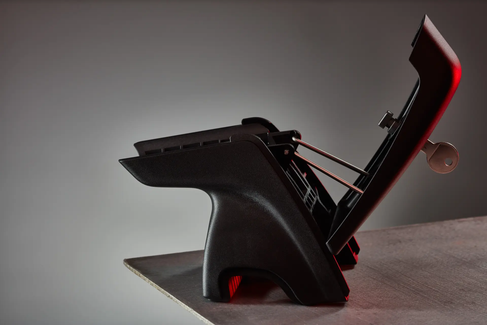 Schwarzes Kunststoffbauteil mit Metallstreben und Schlüssel auf einem Tisch.