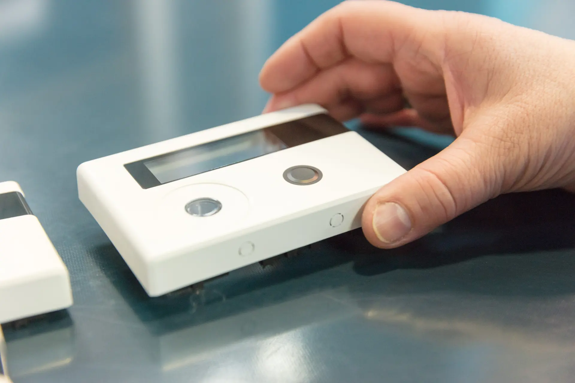 Hand hält ein weißes Gerätegehäuse mit Display und Tasten.