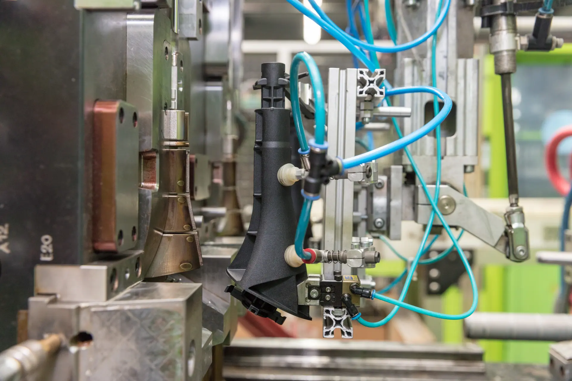 Pneumatische Vorrichtung bearbeitet ein schwarzes Kunststoffteil in der Produktion.