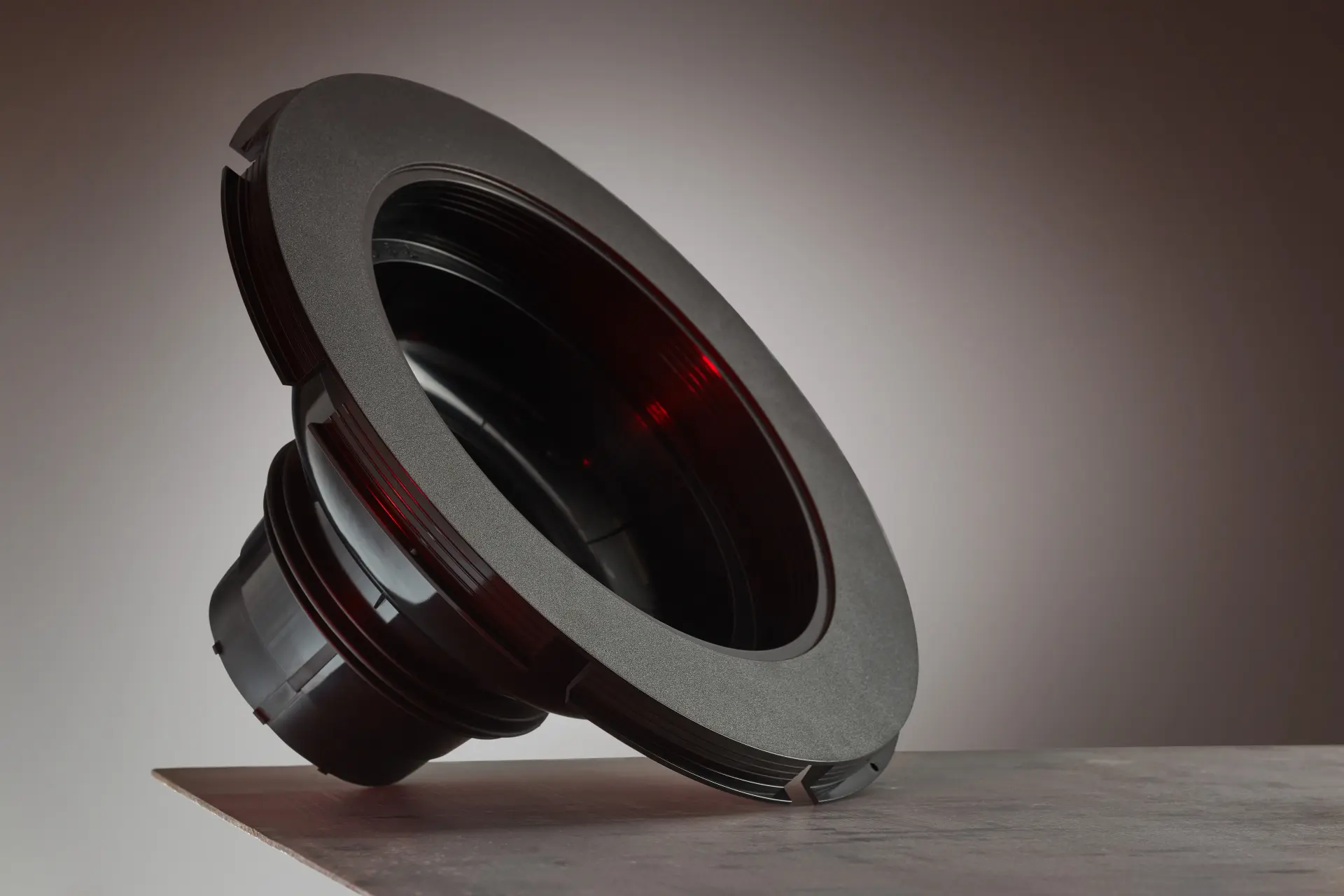 Schwarzes rundes Kunststoff-Bauteil mit Flansch auf einem Tisch.